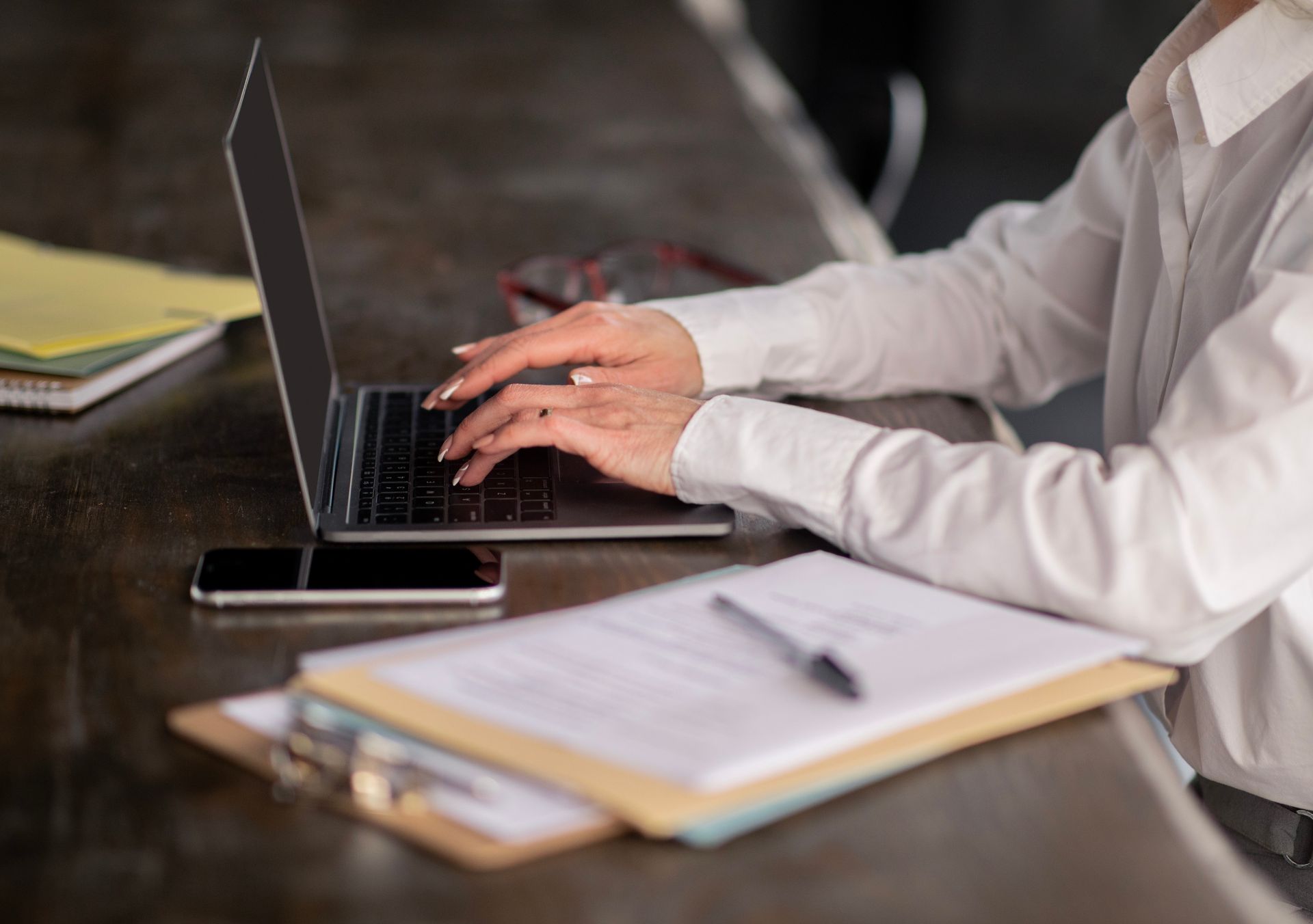 Person typing on a laptop at a desk with notebooks and a pen nearby