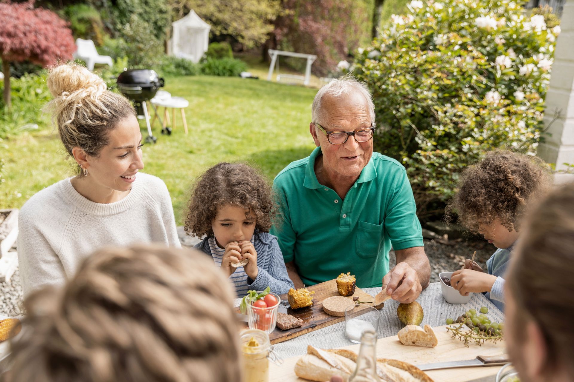 Family sharing food at an outdoor garden table with drinks and pastries
