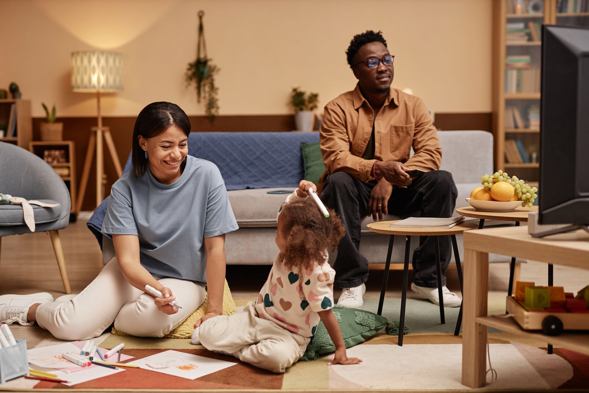 Two people sit on the floor with a dog in a cozy living room, while another person sits nearby.
