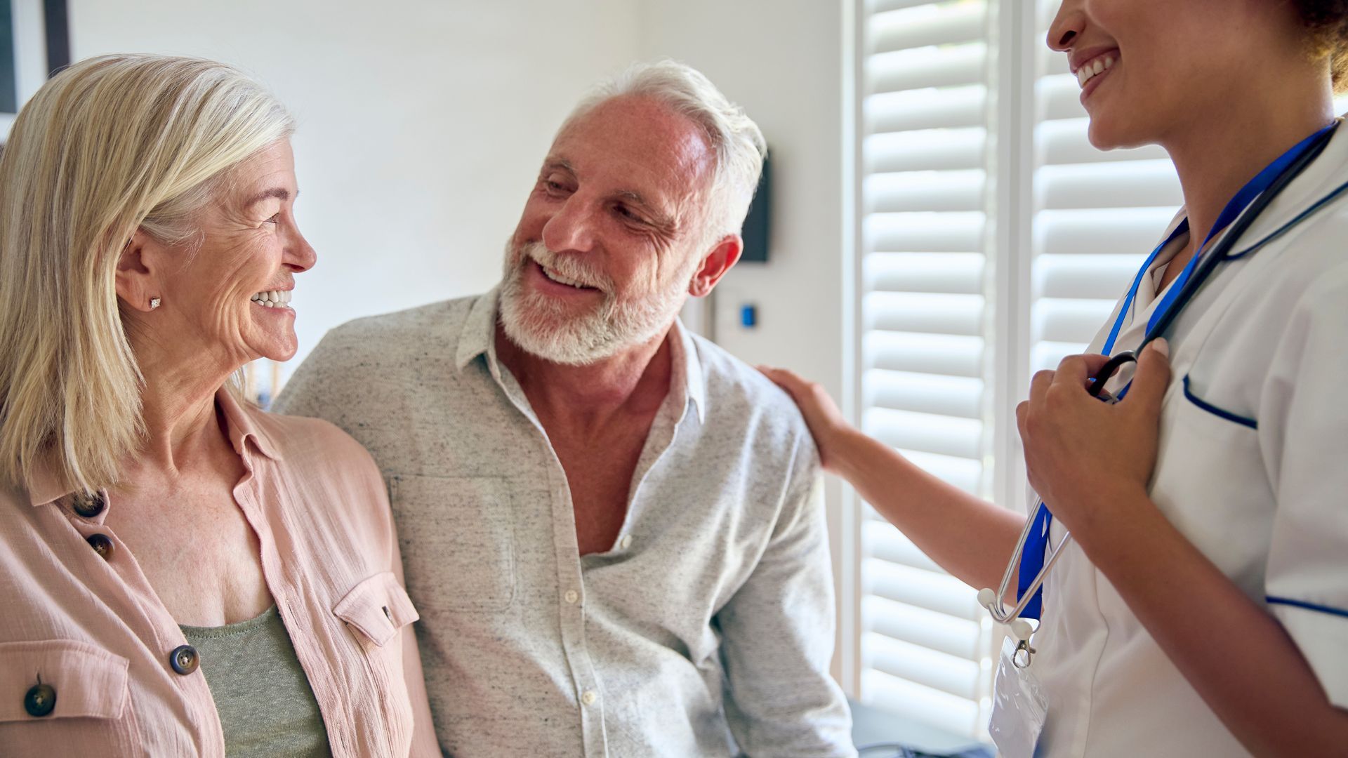 Nurse speaking with smiling patient and companion in a bright clinic room