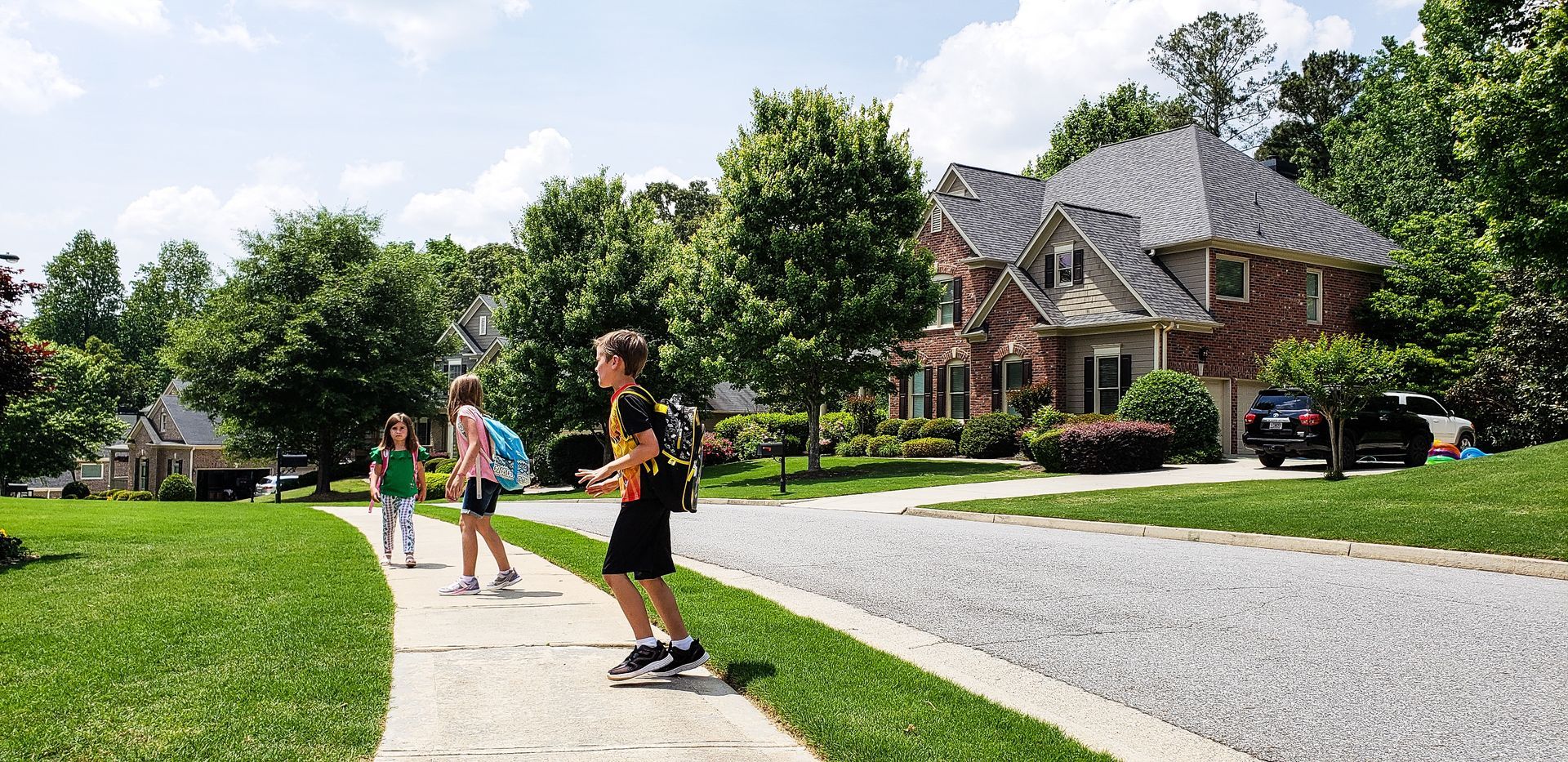 People walking on a suburban sidewalk beside a street and houses on a sunny day