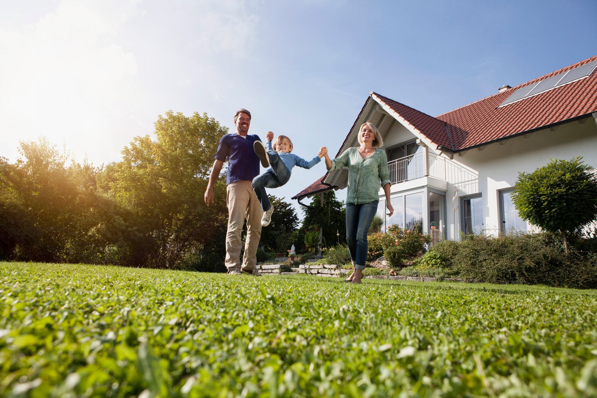 Three people running and smiling on a sunny lawn in front of a white house