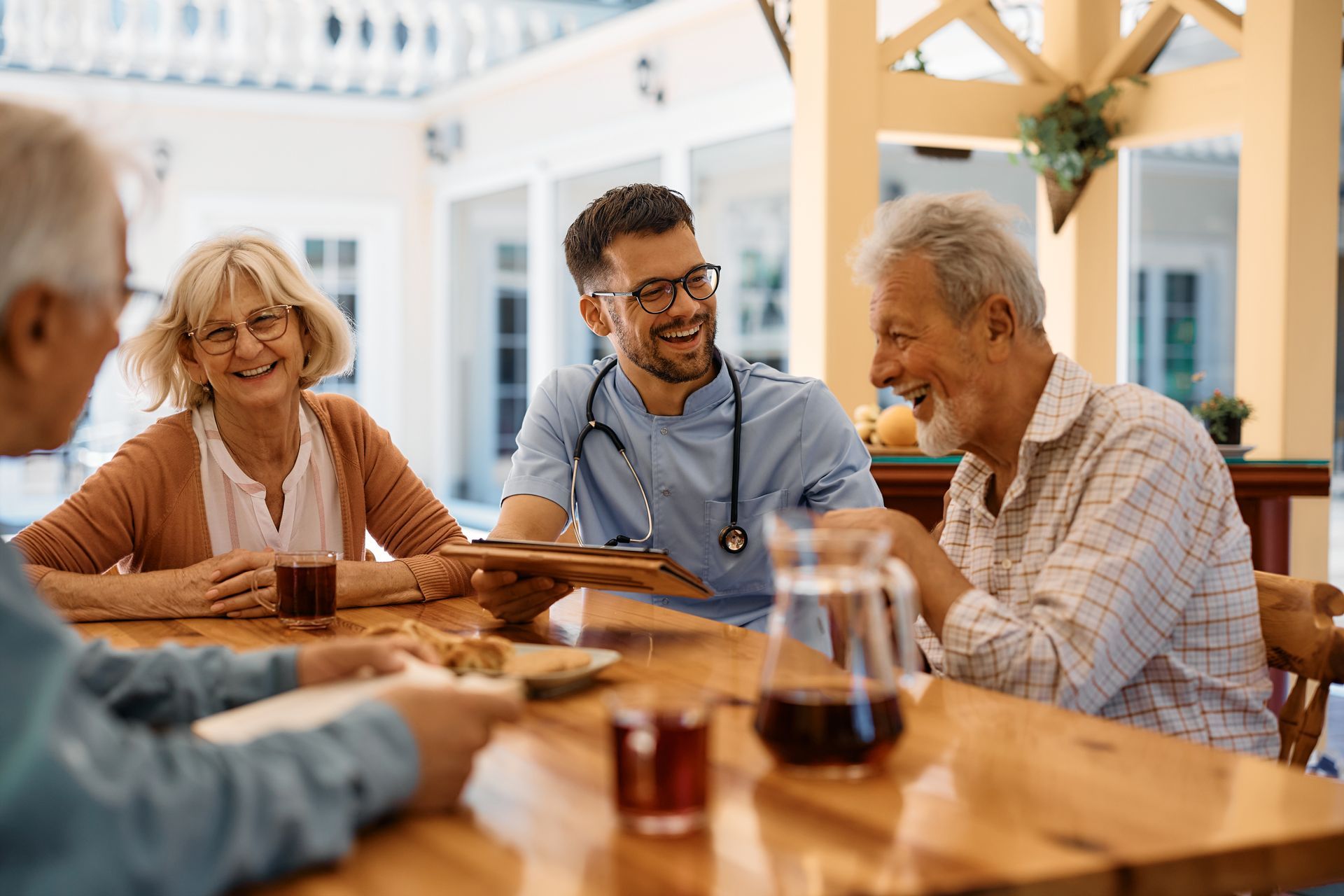 Four friends chatting at a wooden table in a bright café, smiling with drinks and coffee cups.