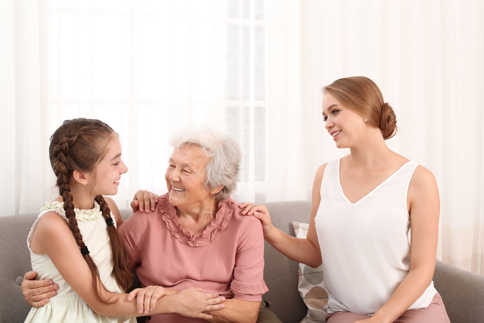Three women sitting together on a couch, smiling and chatting in a bright room