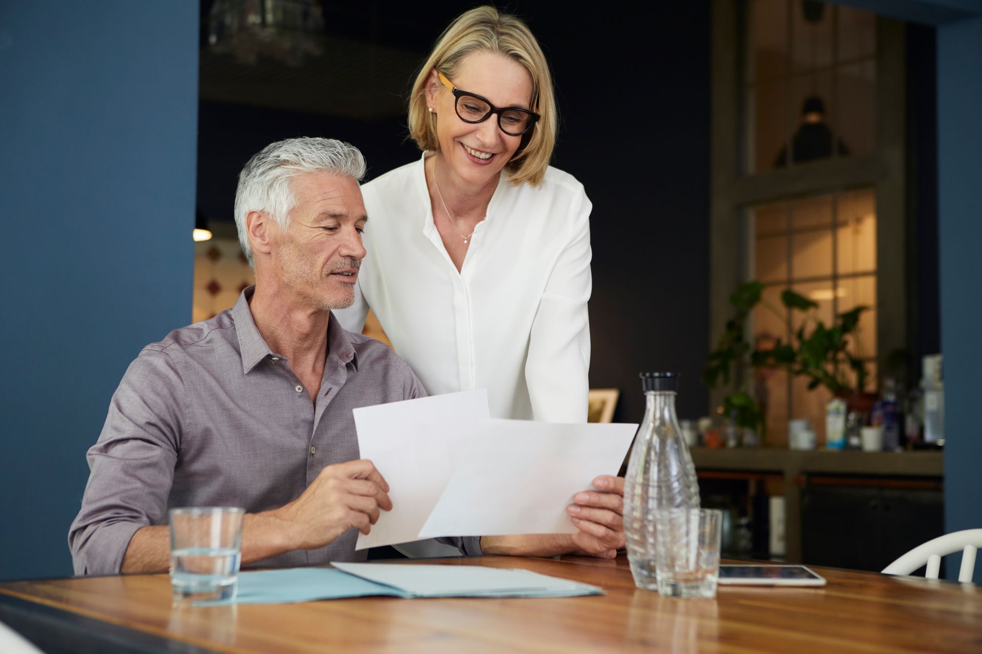 Two people review documents at a table in a modern office, with a laptop and water glass nearby.