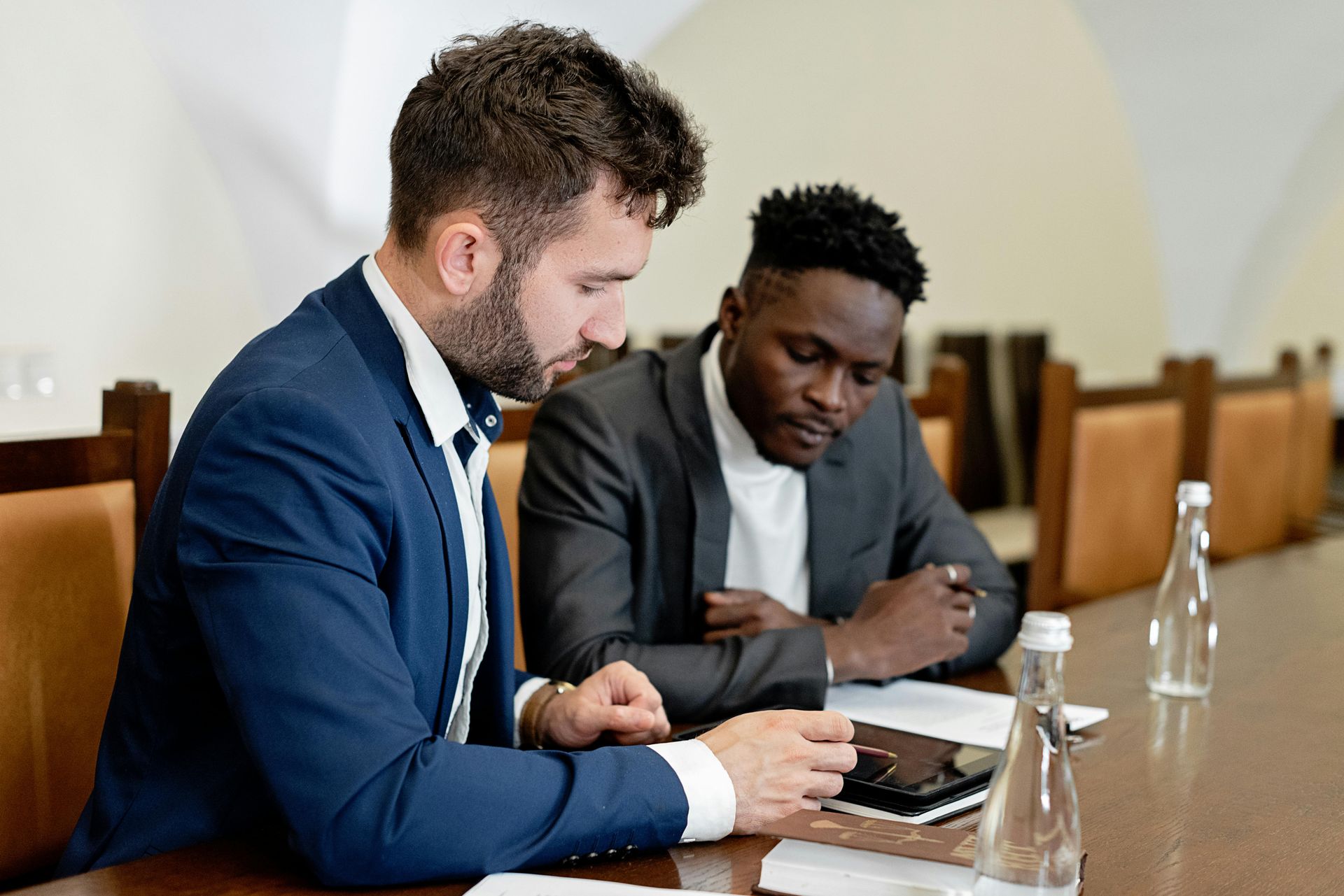 Two men in suits reviewing a laptop at a conference table with water glasses.