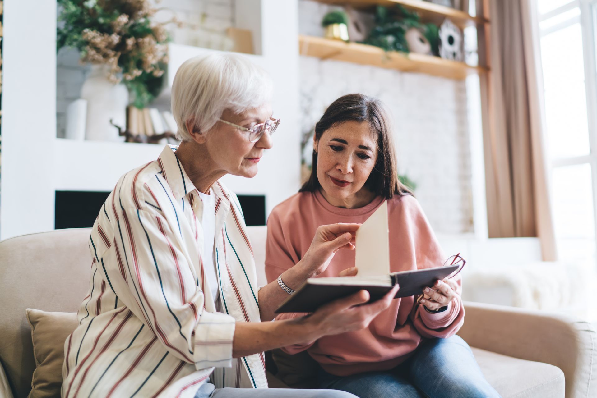 Two people sit on a couch, looking at a tablet and discussing it in a bright living room.