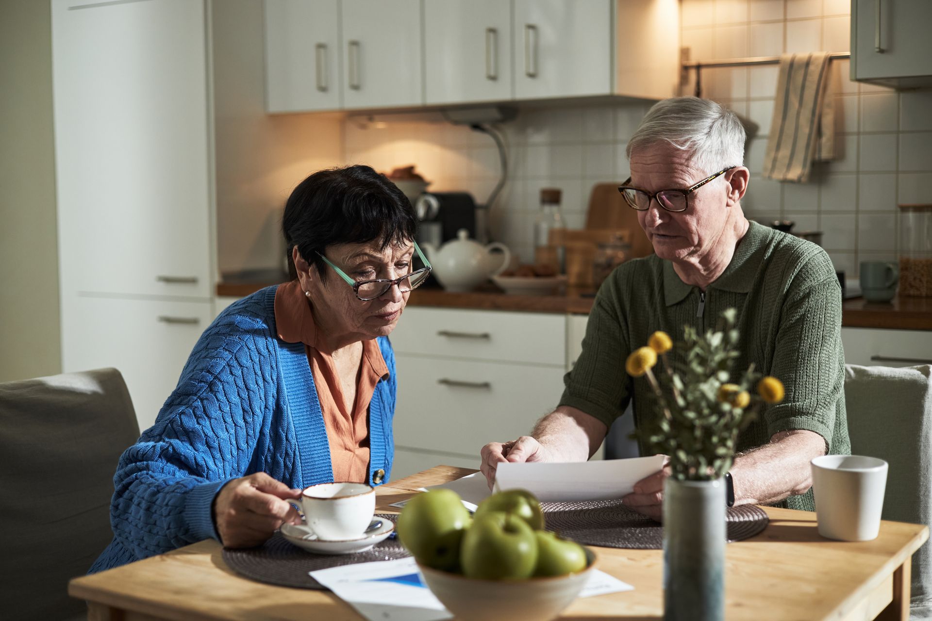 Two people eating at a kitchen table with coffee and fruit bowls in a bright home kitchen