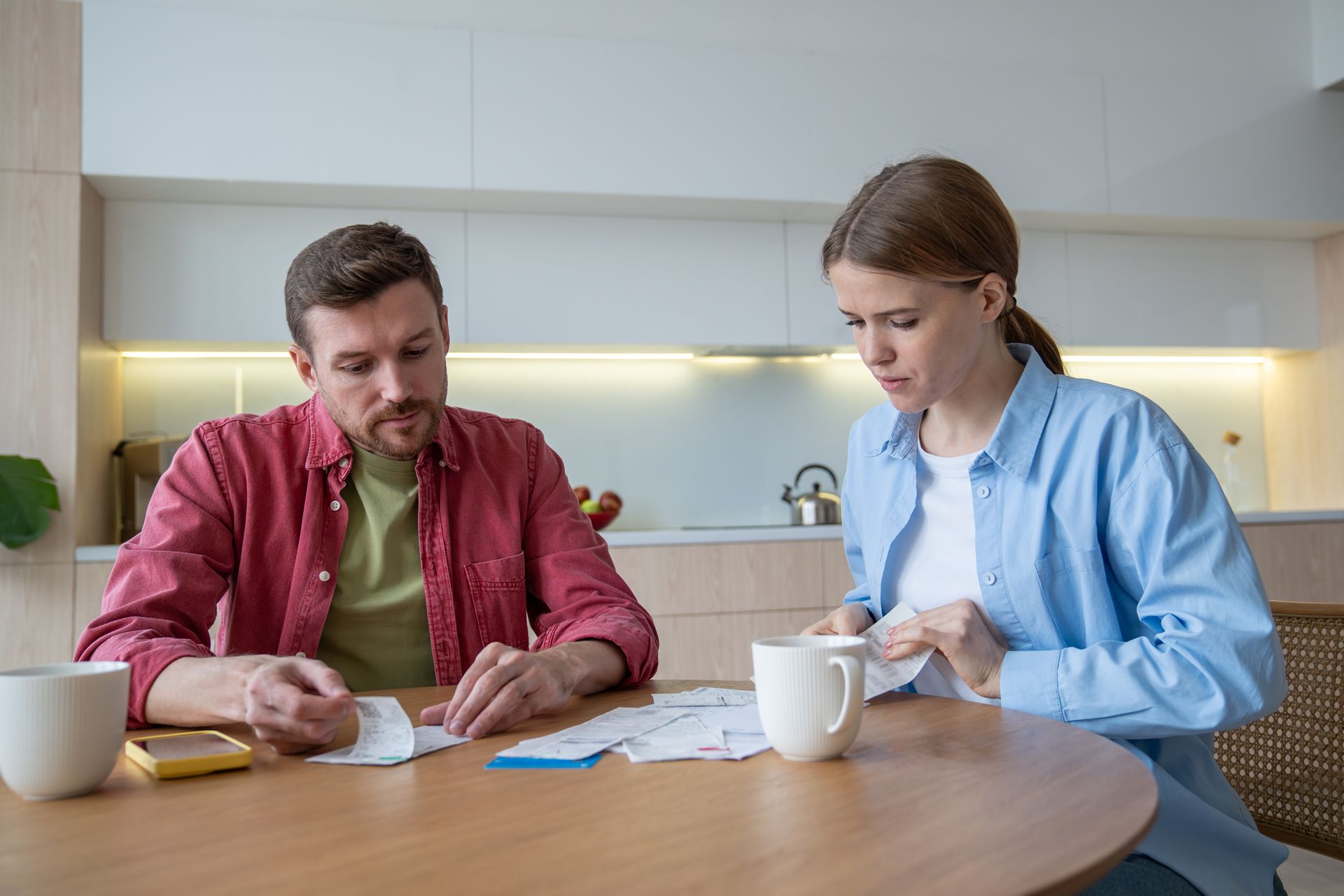 Two people reviewing papers at a kitchen table with mugs in a bright modern home