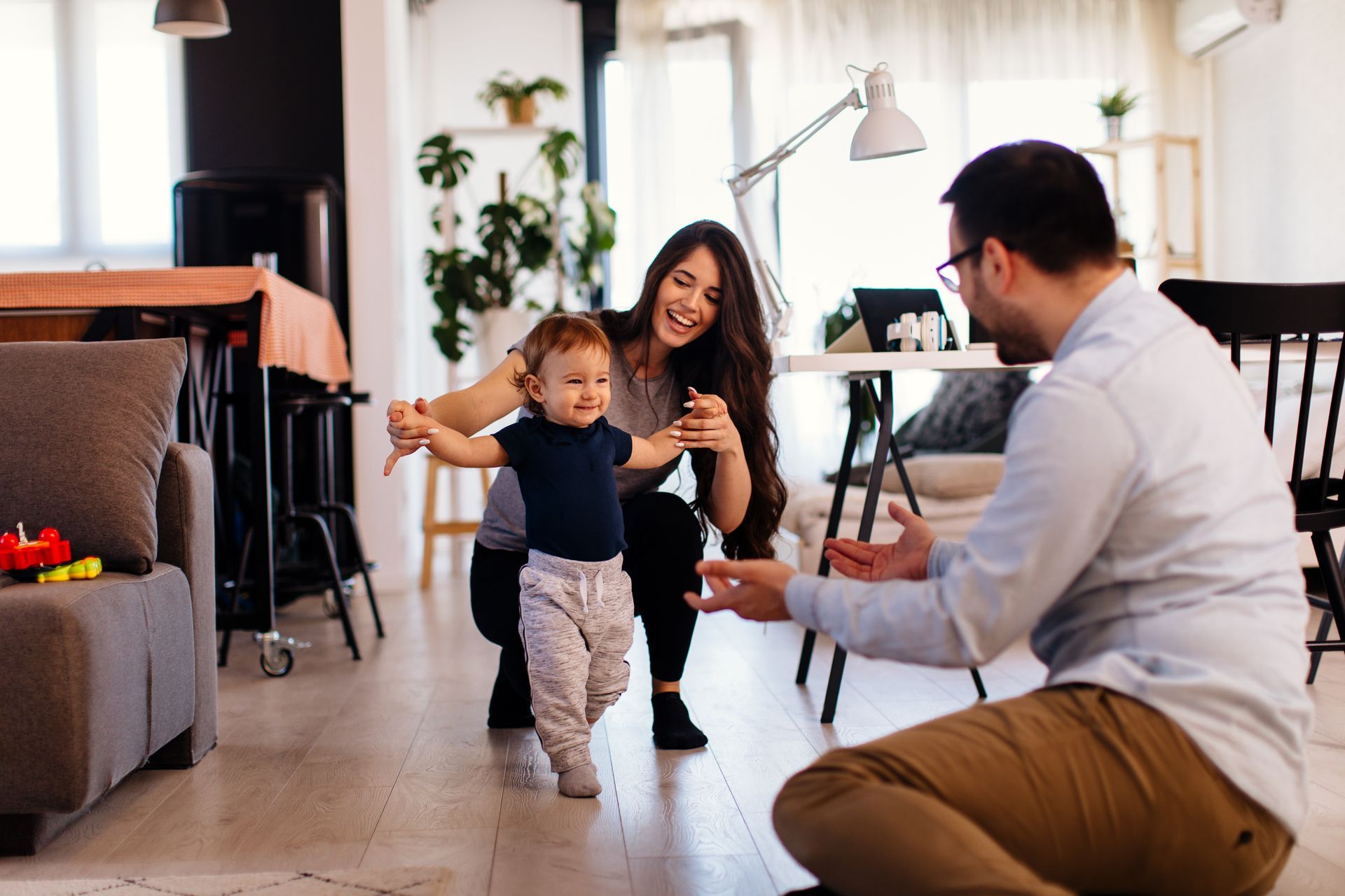 Parent and child playing in a bright living room while a seated man watches and gestures nearby