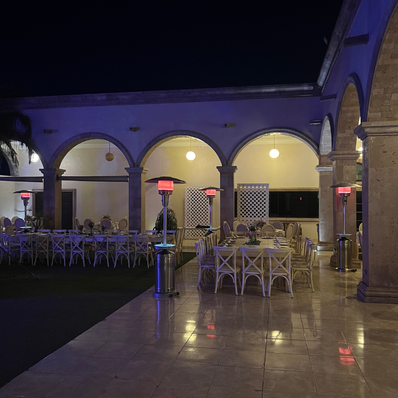 Un patio con mesas y sillas y calentadores por la noche.