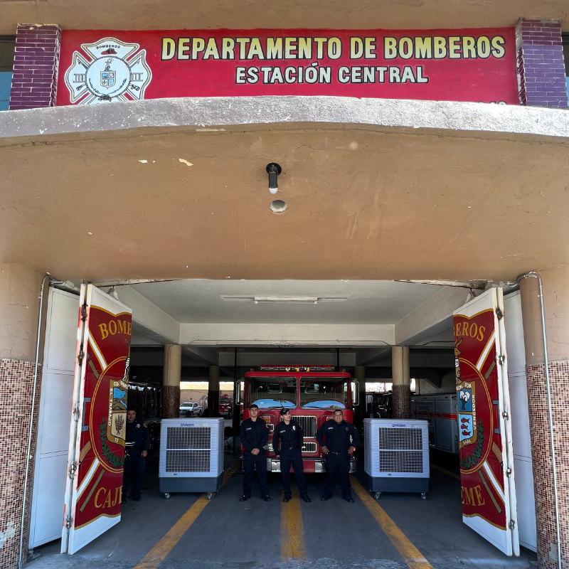 Departamento de bomberos estacion central, al centro un camión de bomberos, 3 persona y 2 aerocoolers.