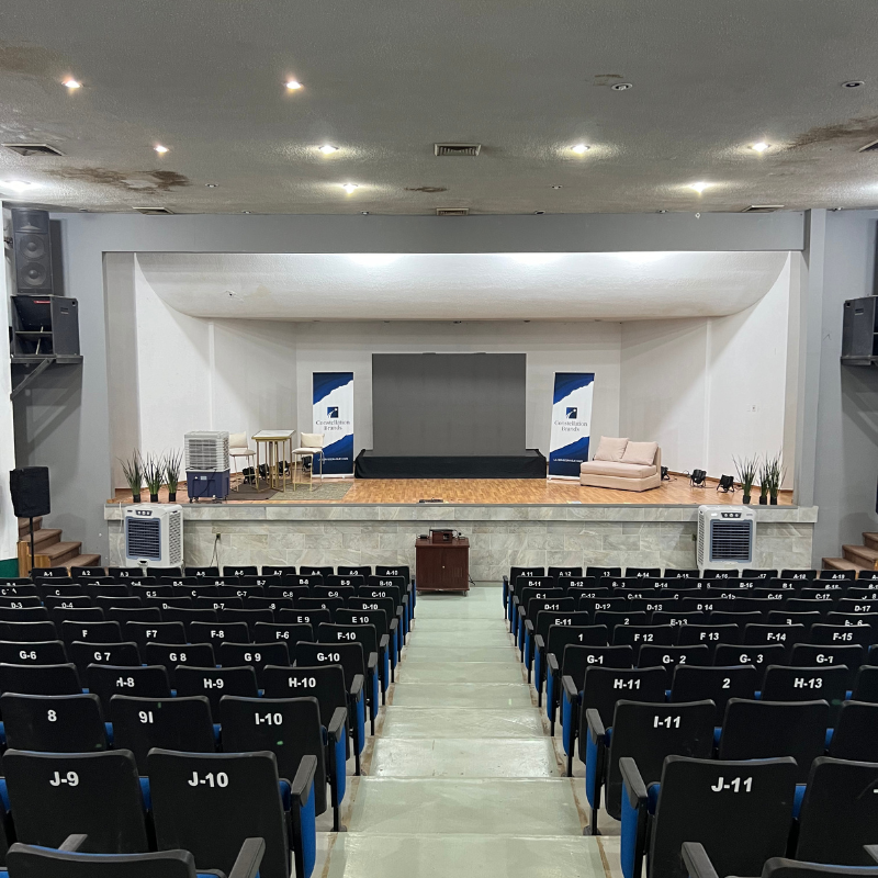 Un gran auditorio con filas de asientos y un escenario y 2 aercoolers.