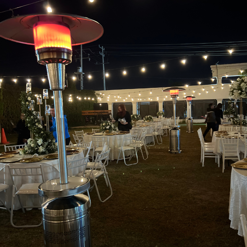 Se preparan mesas y sillas para una recepción de boda, al frente un calentador portátil.
