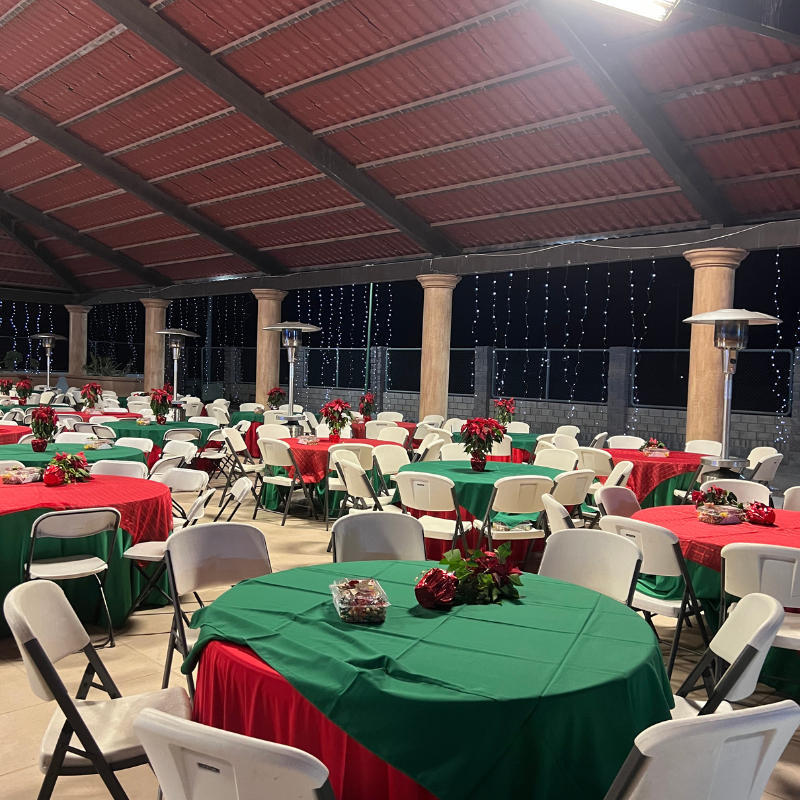 Una salón de fiesta con mesas y sillas preparadas para una fiesta y alrededor varios calentadores portátiles