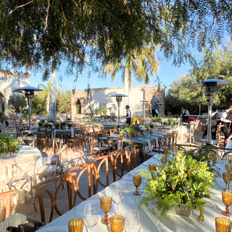 Un gran comedor al aire libre con mesas y sillas  para una recepción de boda y varios calentadores portátiles alrededor