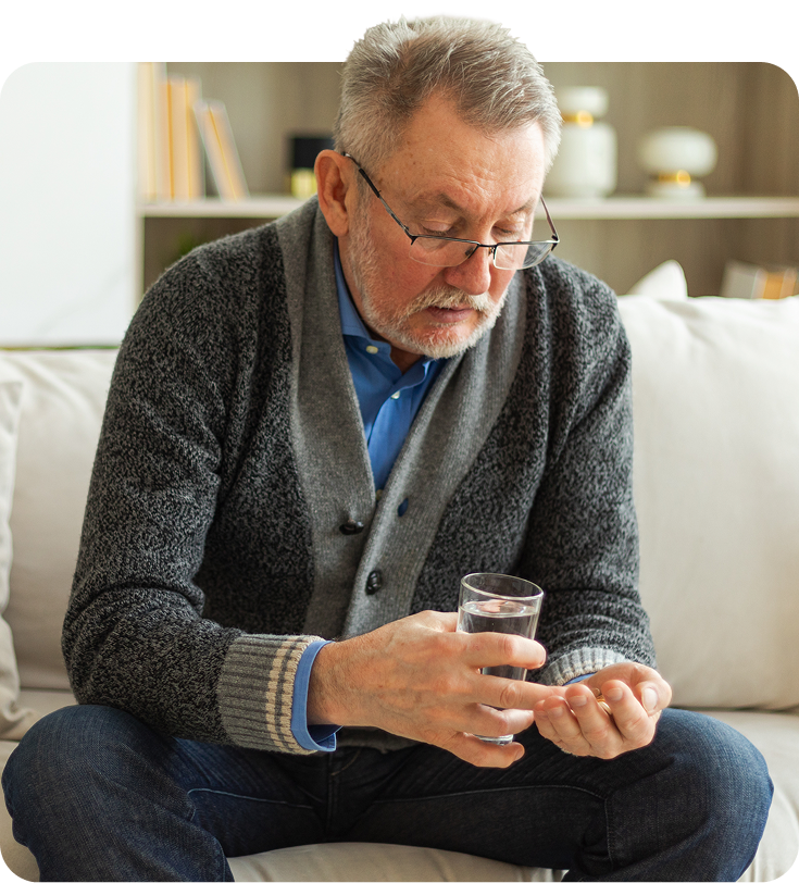 Man holding pills and glass of water, sitting on a couch.