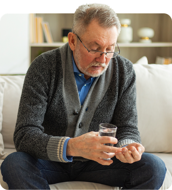 An elderly man is taking a pill with a glass of water