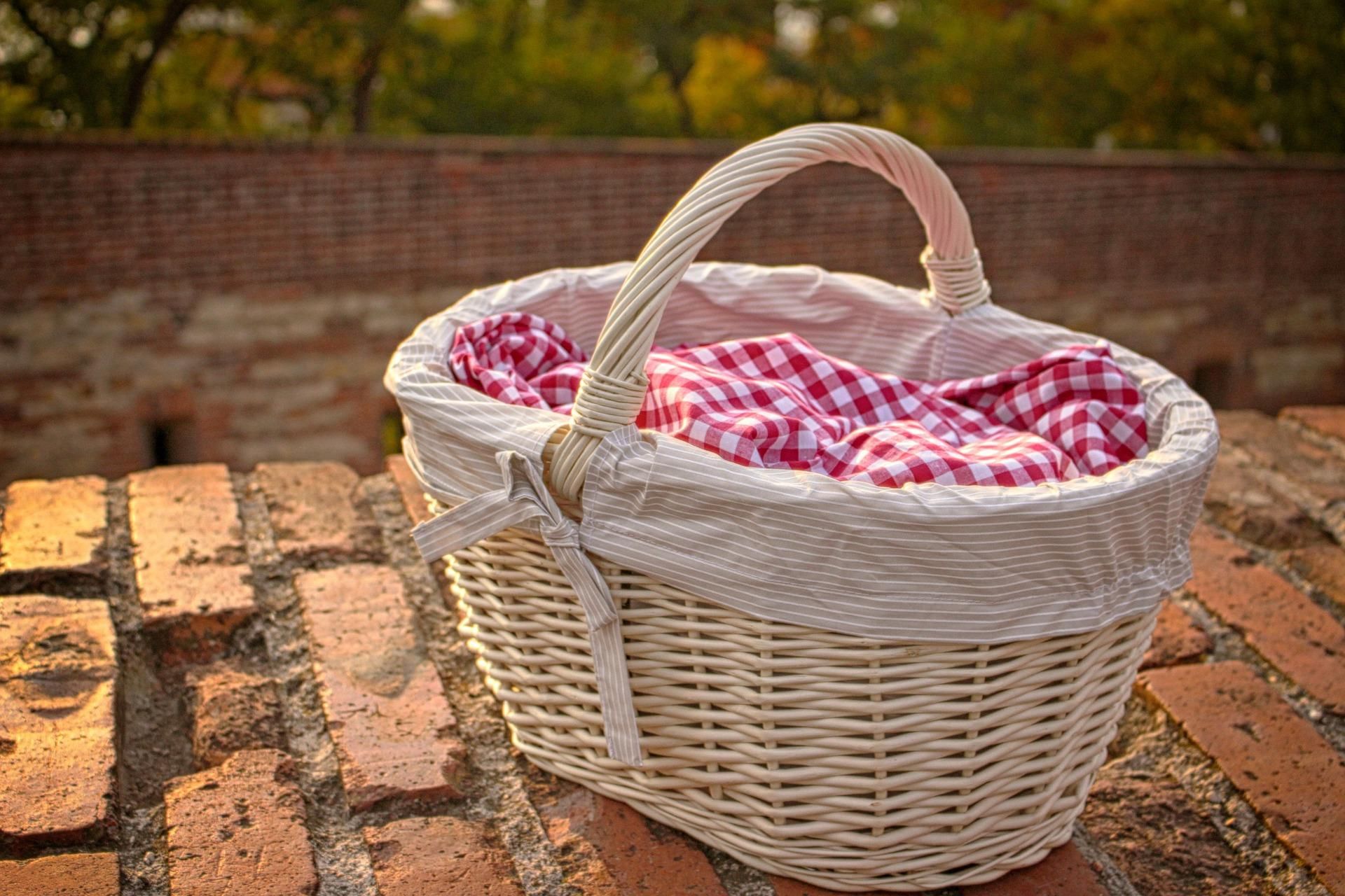 Wicker picnic basket with red and white checkered cloth on a brick wall.