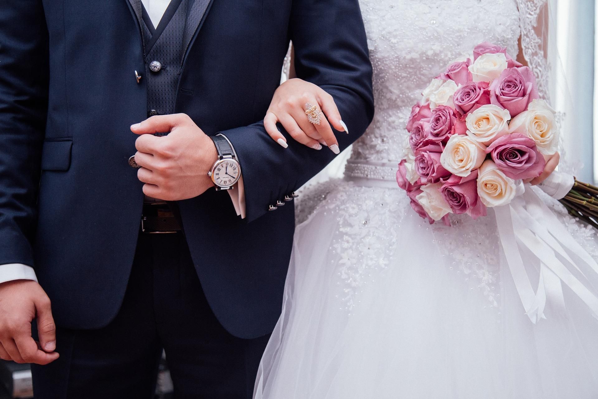 Bride and groom; he in a navy suit, she in a white wedding gown, holding a pink and white bouquet.