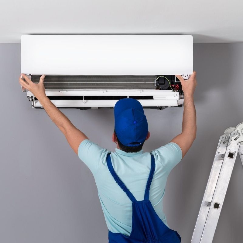 Técnico instalando un aire acondicionado mural en el interior de una vivienda, con una escalera a su lado.