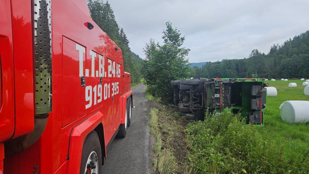 En rød bergingsbil i nærheten av et veltet grønt kjøretøy på et jorde ved en vei.