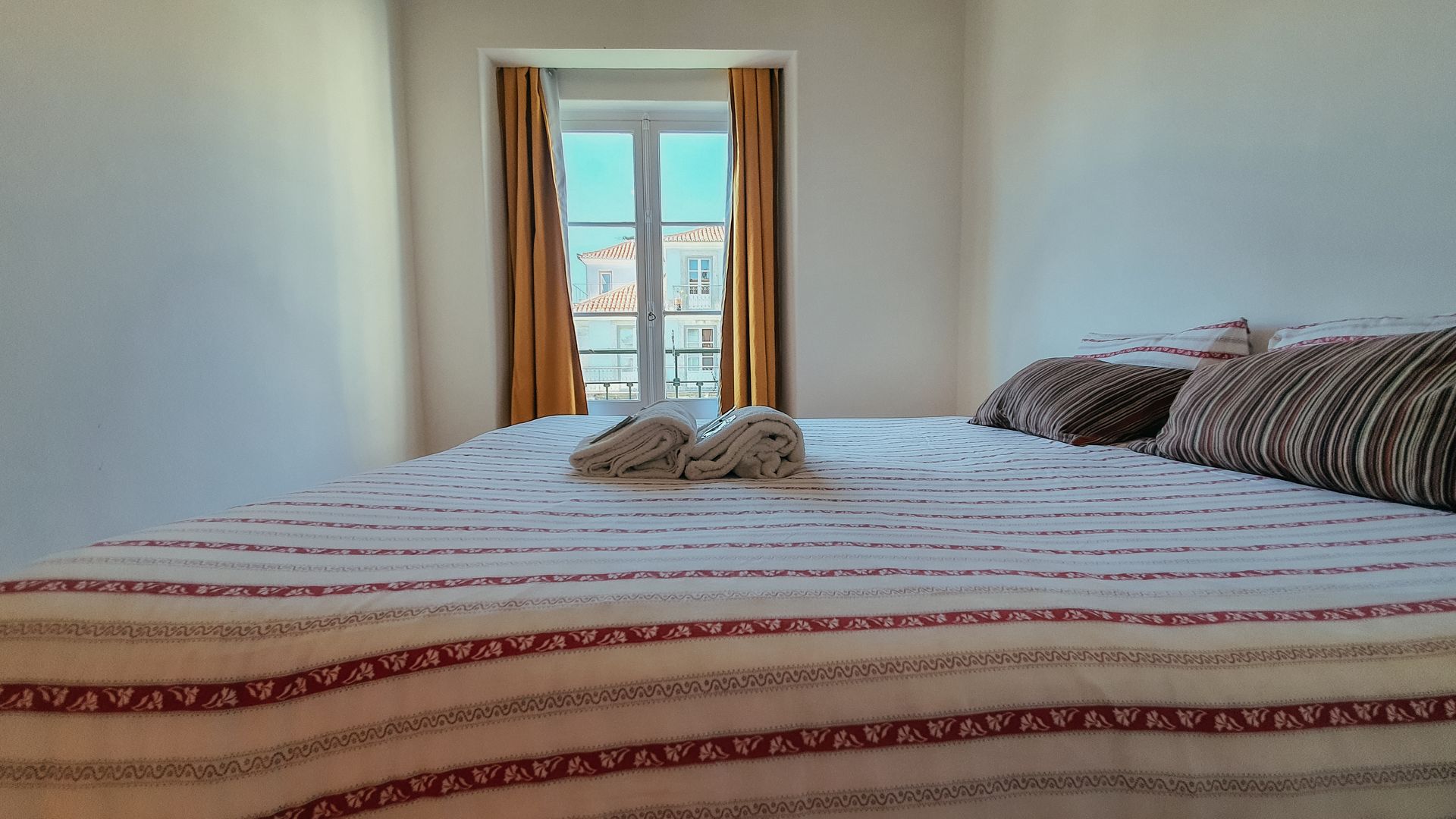 A bed with a striped blanket and pillows in a bedroom with a window.