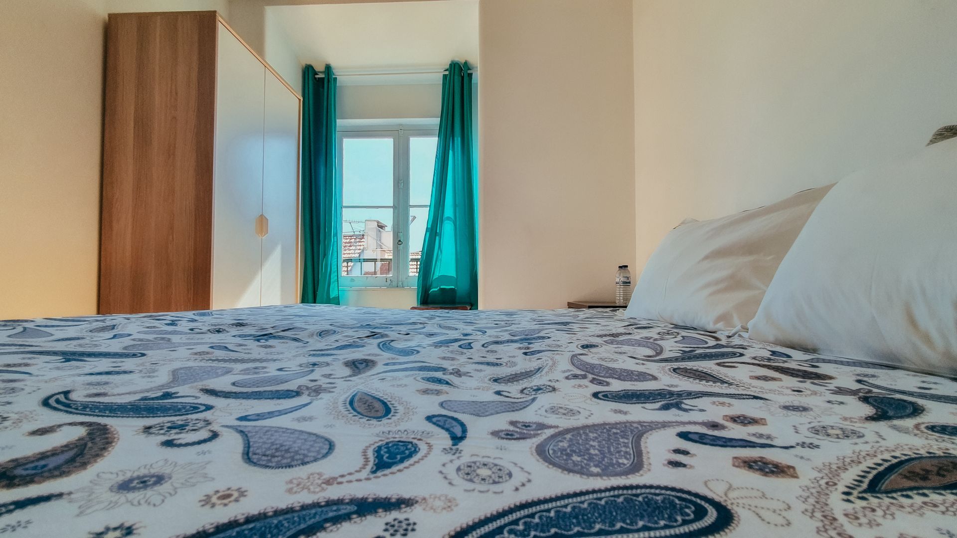 A bed with a blue and white blanket in a bedroom with a window.