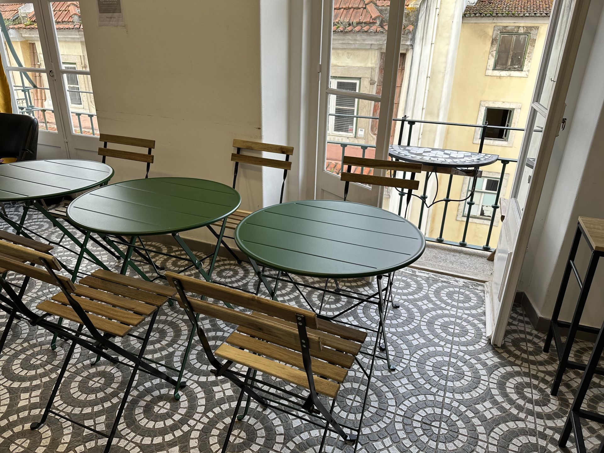 A room with green tables and chairs and a balcony.