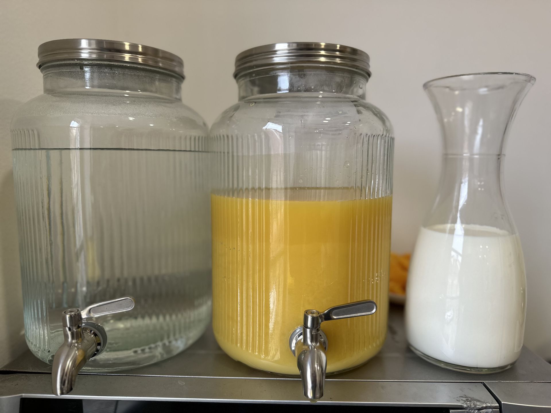 Three jars of liquid are sitting on a shelf next to a pitcher of milk.