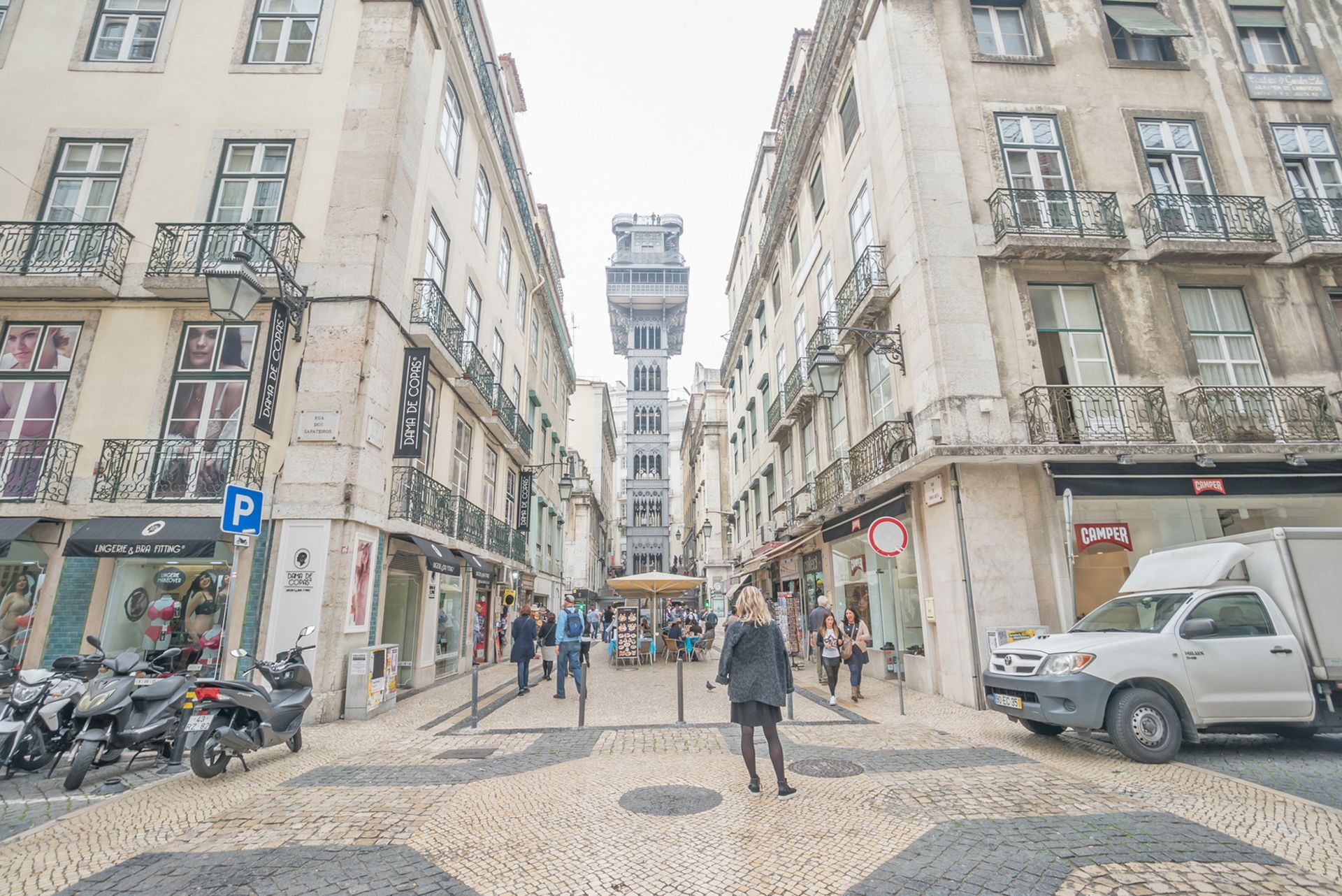 A woman is walking down a narrow street between two tall buildings.