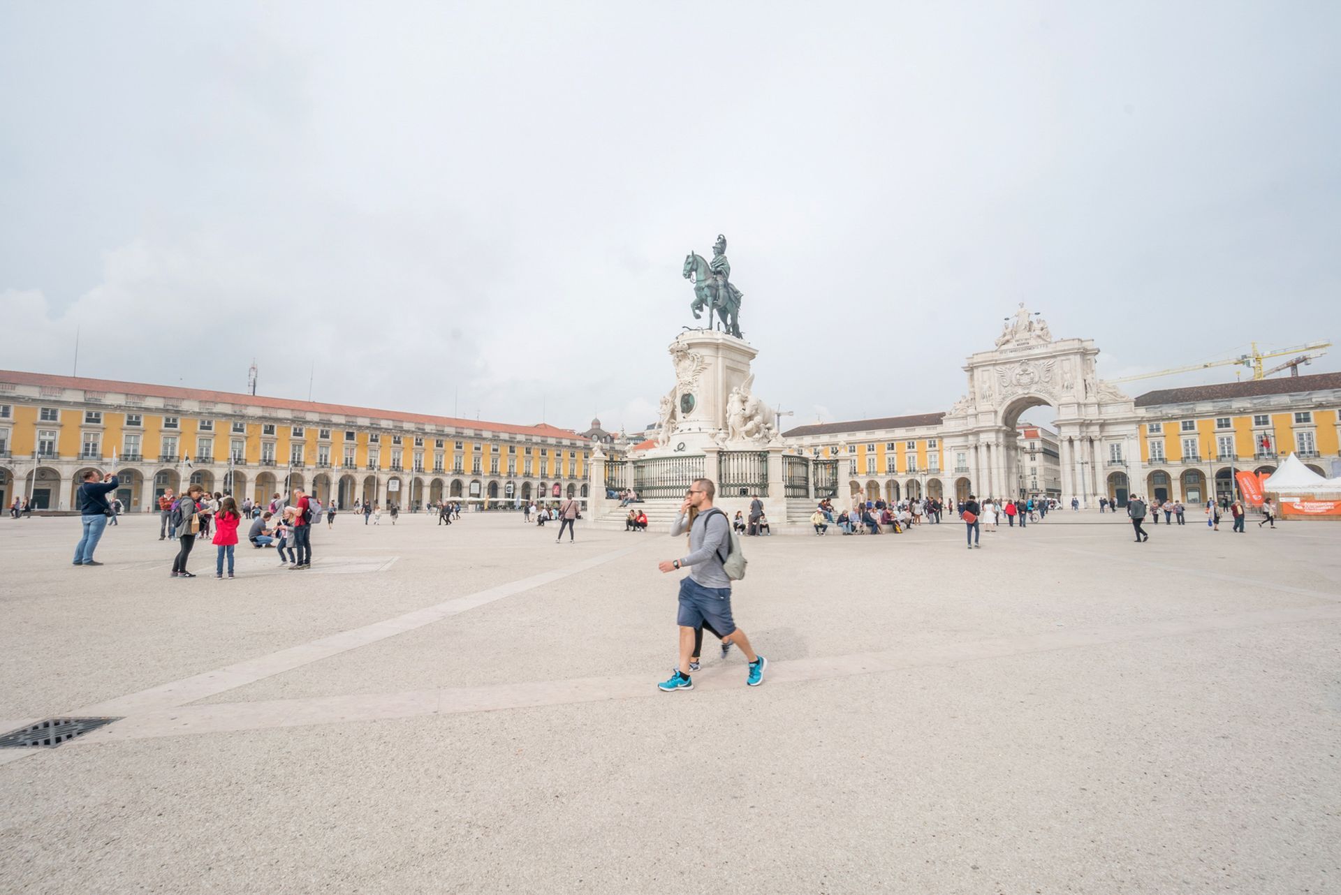 A man is running in a square in front of a statue of a man on a horse.