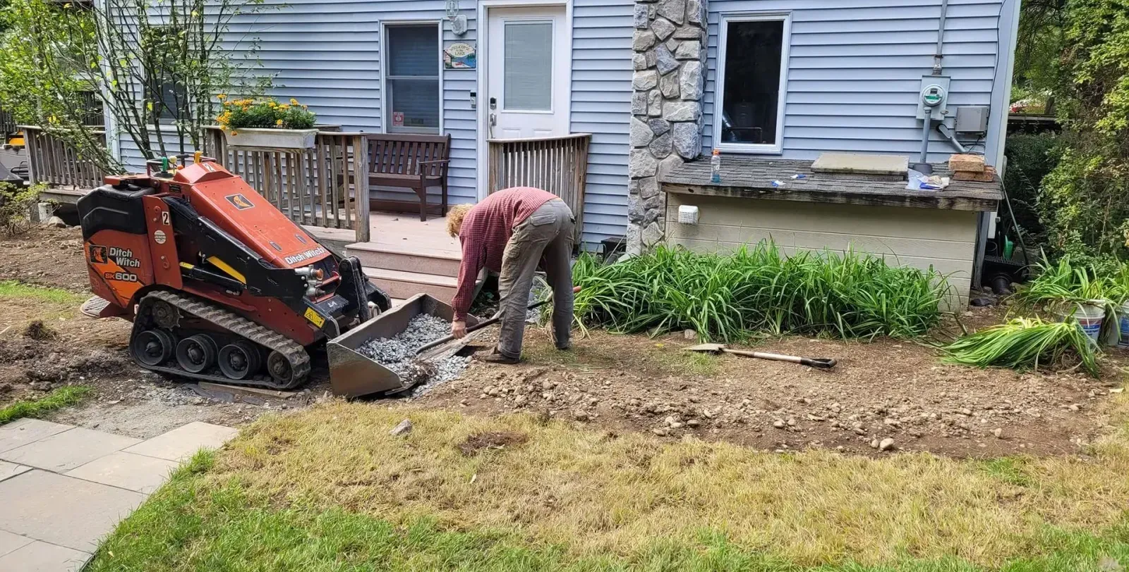 A man is digging in the dirt in front of a house.
