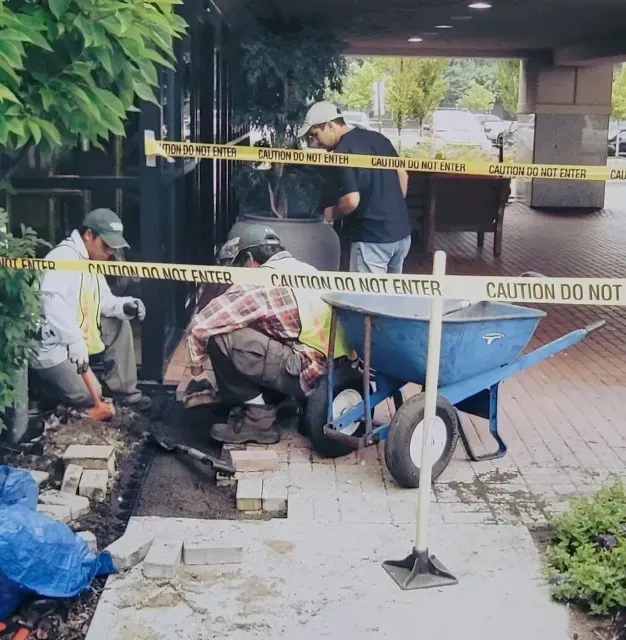 A group of men are working on a sidewalk in front of a caution tape