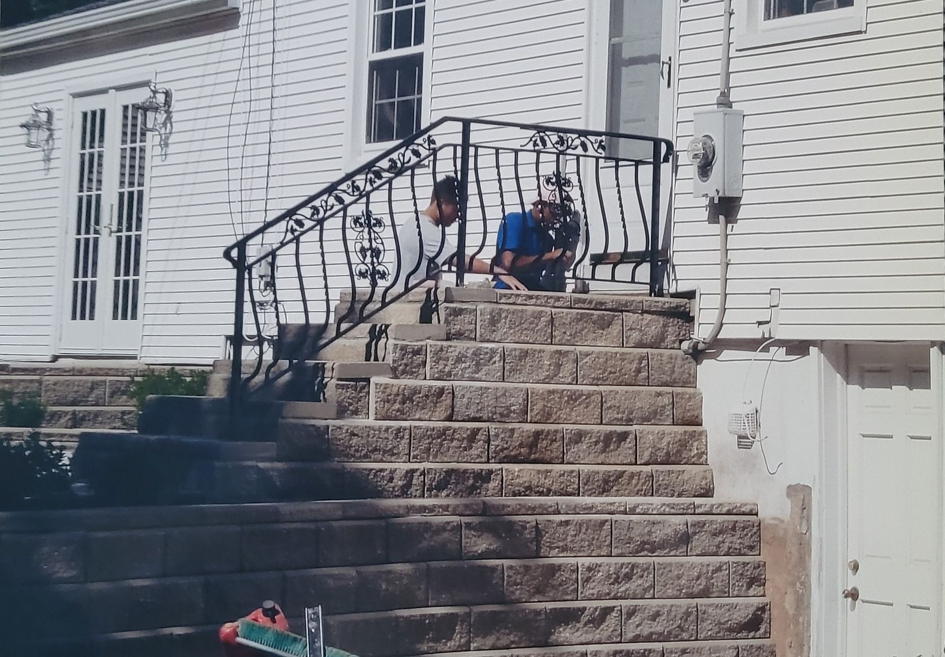 A man is sitting on the steps of a house with a wrought iron railing.