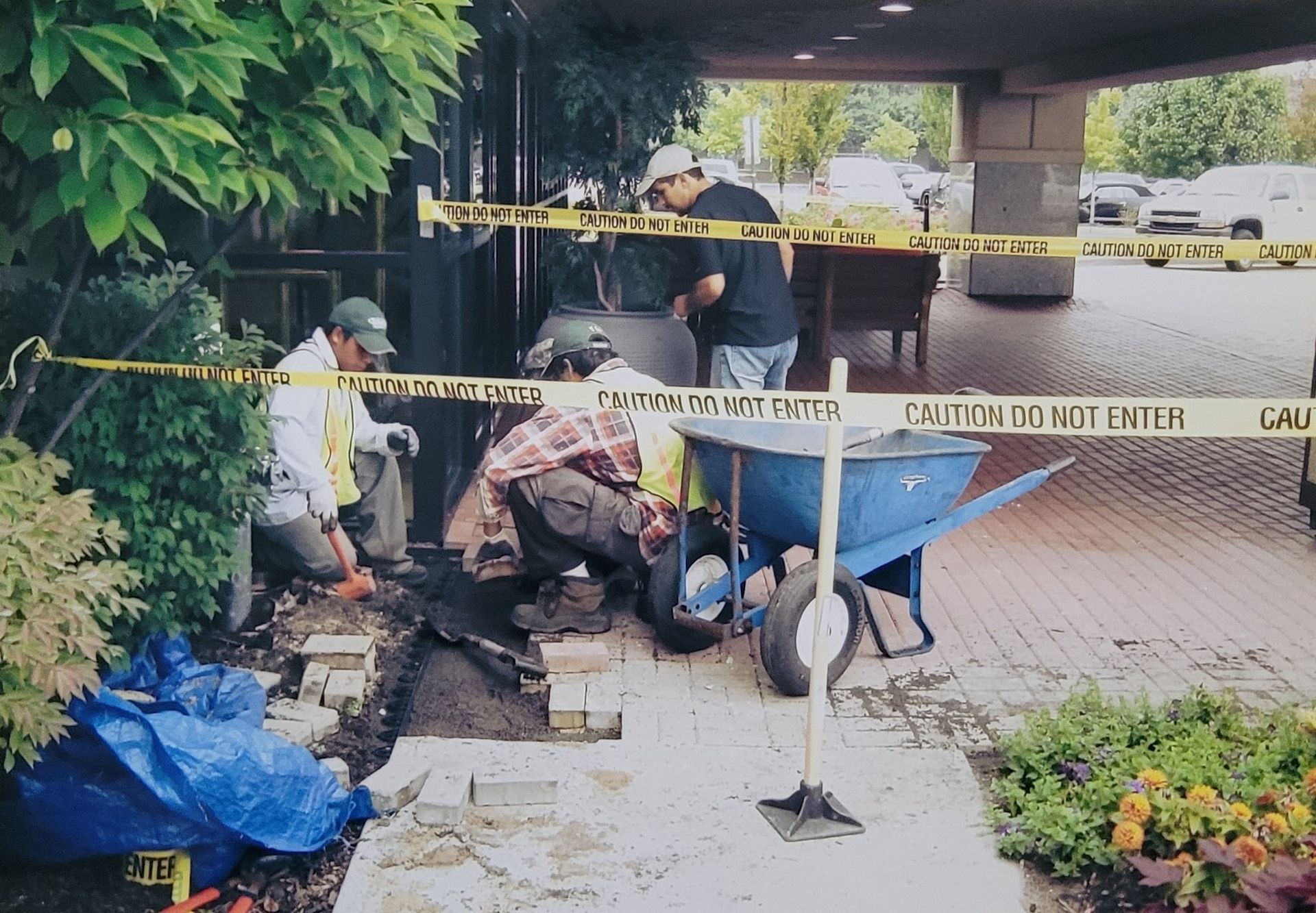 A group of men are working on a sidewalk in front of a caution tape