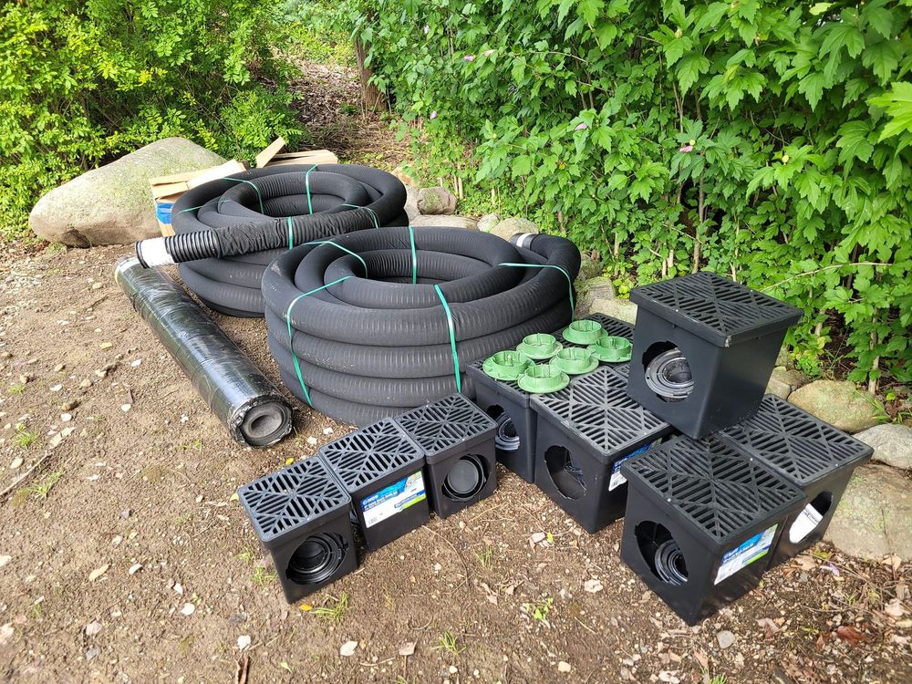 A pile of drainage equipment is sitting on the ground next to a bush.