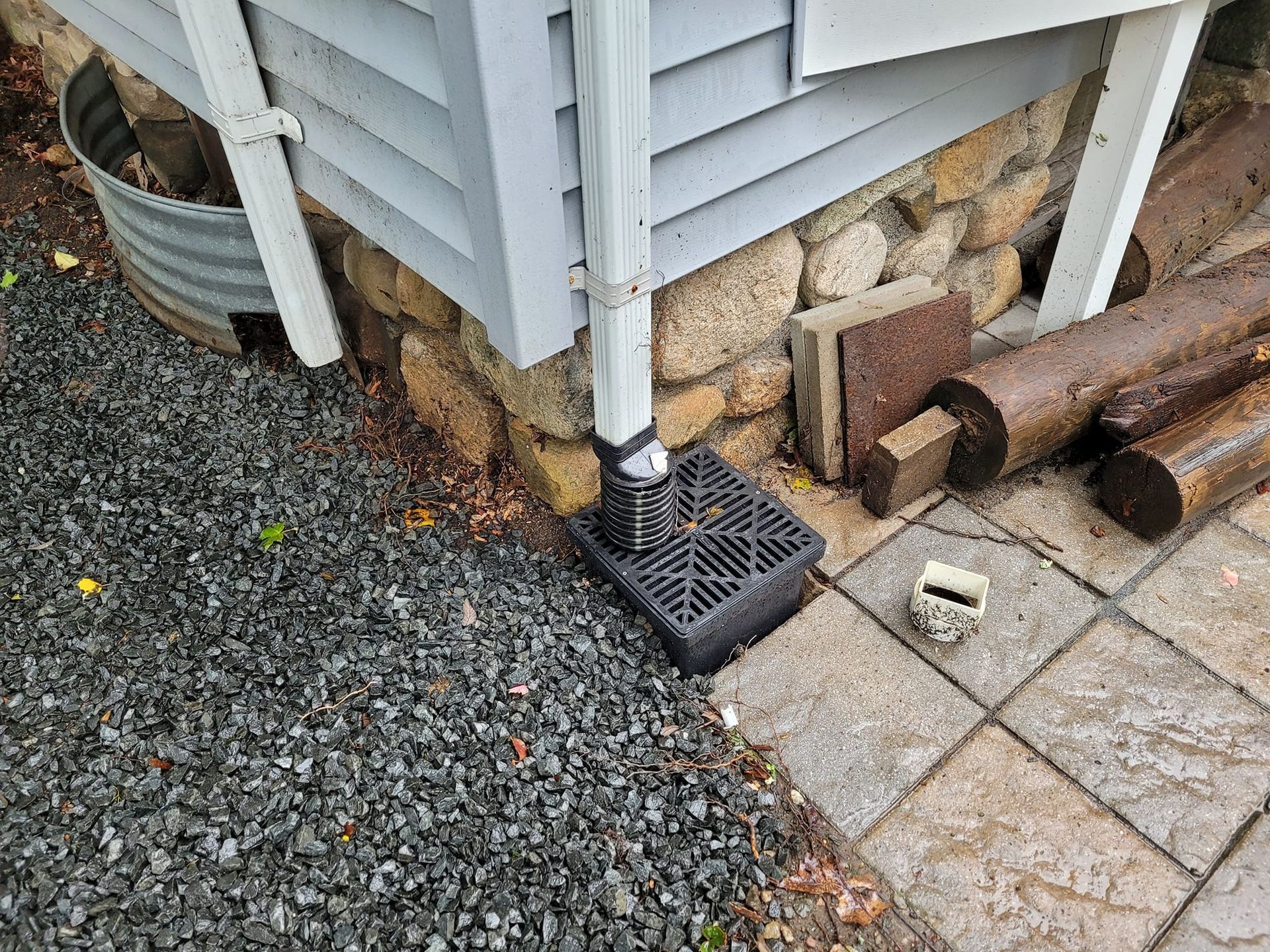 A drainpipe is sitting on the side of a house next to a stone wall.