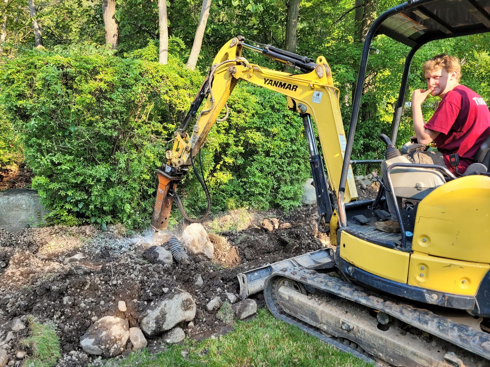 A man is driving a yellow excavator in a yard.