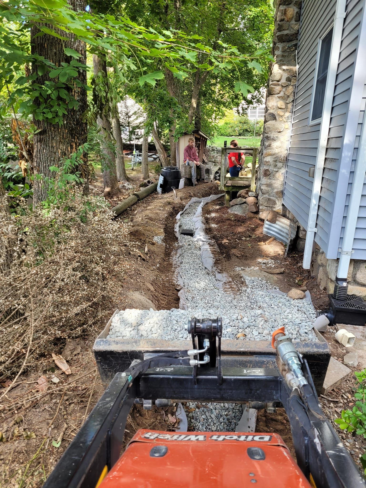 A tractor is driving down a dirt path next to a house.