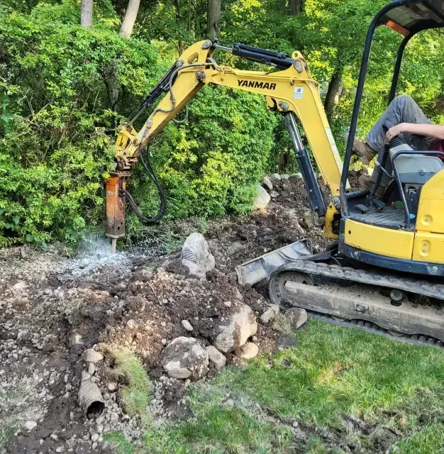 A man is driving a yellow excavator on a dirt road.