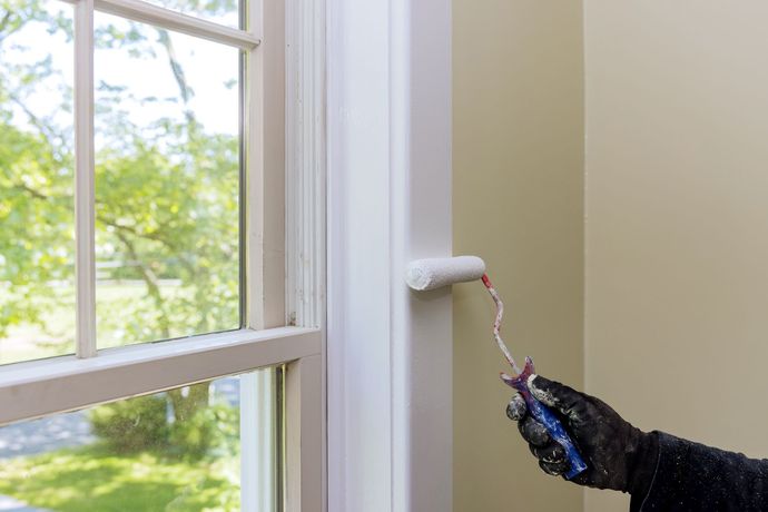 A person is painting a window frame with a roller.