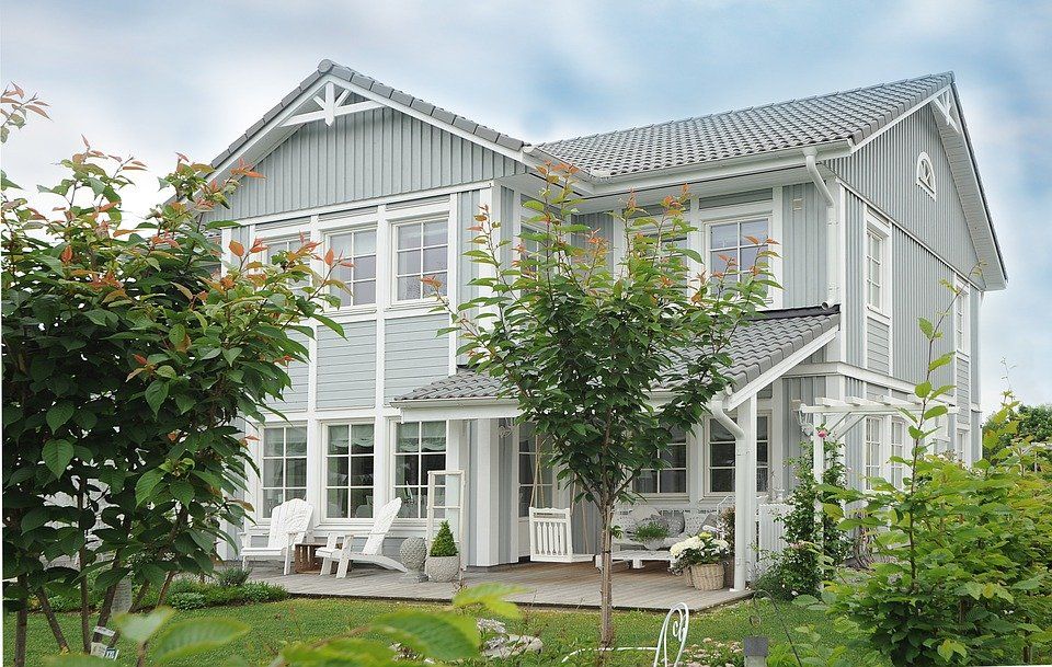 Two-story house with gray siding, white trim, and a porch, set in a green yard with trees.