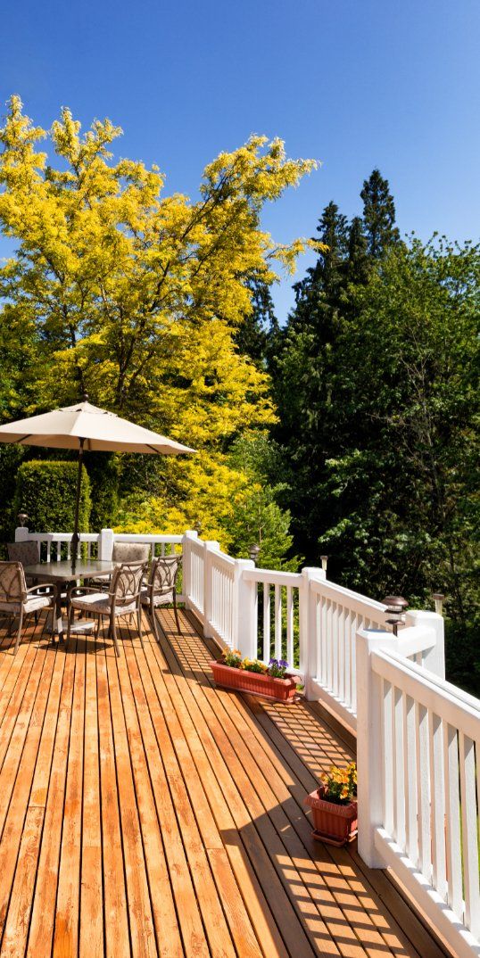 Backyard deck attached to a house.  The deck has a patio table and chairs, flower boxes and a long white wooden railing.