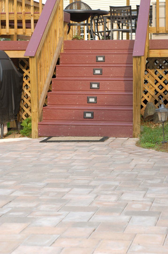 Stairs leading from a backyard deck to a stone patio. The deck stairs are dark brown and so are the railings.