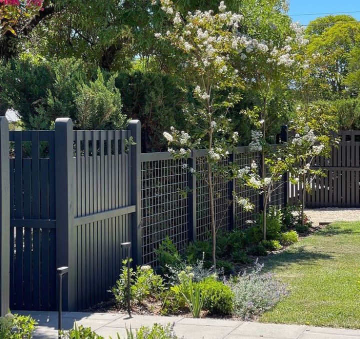 Large black fence in a backyard.  Gardens line the fence.  It is a mixture of a wooden fence and metal fencing.