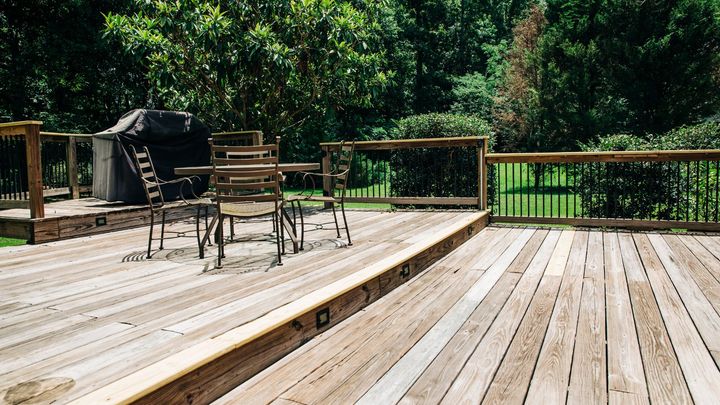 Two-level deck overlooking a large grassy backyard.  The deck has a patio set on it and a barbeque.