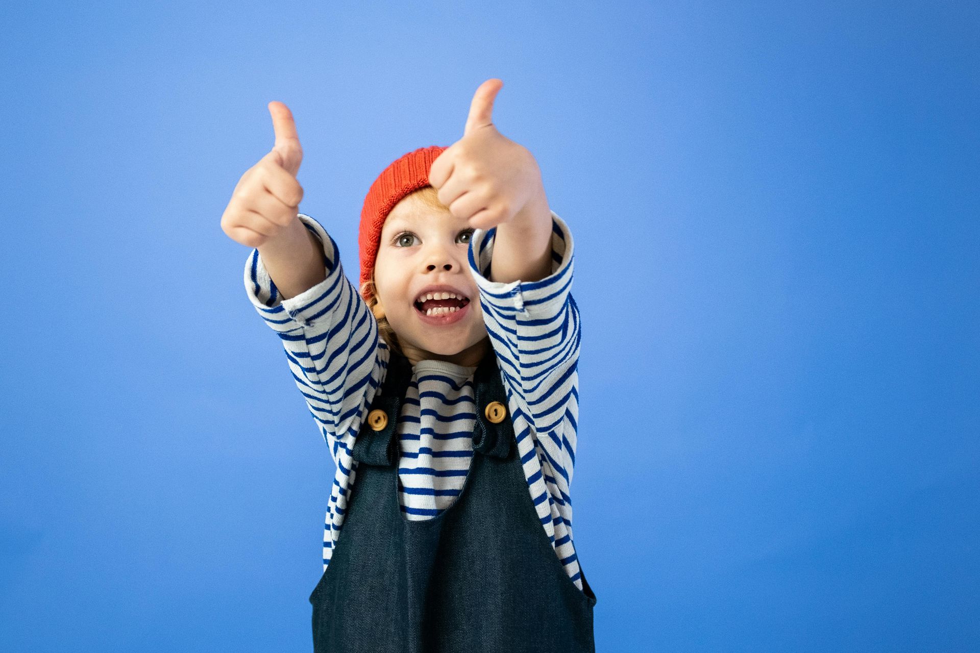 Child with red cap on giving two thumbs up.