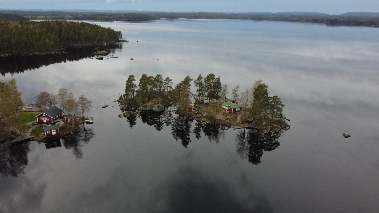 Isla en el lago, con árboles y edificios, agua oscura, cielo nublado.