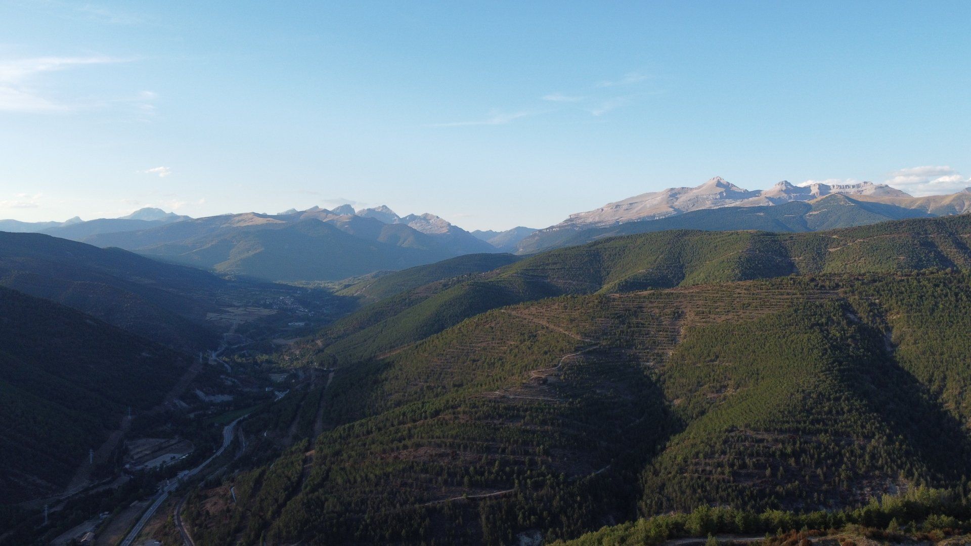 Montañas cubiertas de árboles bajo un cielo azul claro. Un río serpentea por el valle.